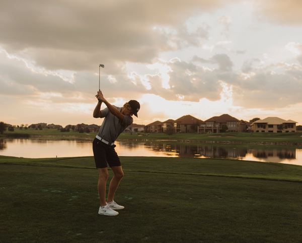 Man swings golf club by water